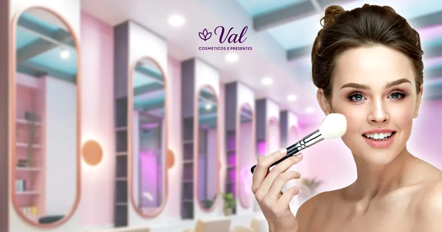 Mulher sorrindo enquanto usando um pincel de maquiagem para aplicar blush na maçã do rosto. Ao fundo, um salão de beleza moderno e desfocado em tons de rosa, com o logotipo da Val Cosméticos e Presentes centralizado no topo.