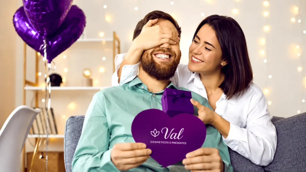 Mulher de camisa branca cobrindo os olhos do namorado para fazer uma surpresa. O homem segura um coração roxo com a marca Val Cosméticos e Presentes e uma caixinha de presente. Balões de coração roxos aparecem ao fundo.